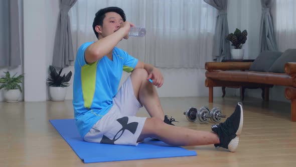 Asian Man Drinking Water After Exercises At Home In Living Room