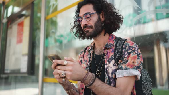 Positive curly-haired bearded man in eyeglasses texting on phone