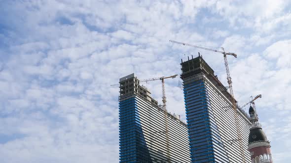 Construction of a Modern Skyscrapers Using Tower Cranes. Timelapse, Moving Clouds on Blue Sky alt