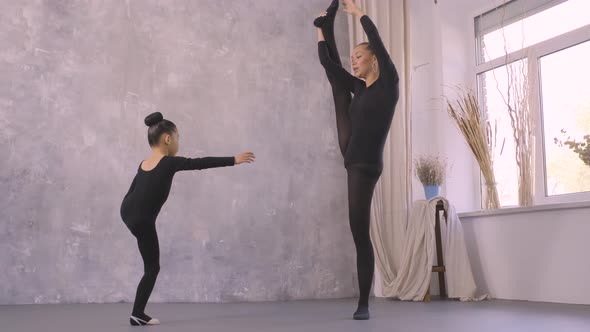 Little Asian Girl in Black Bodysuit Doing Stretching Exercises with the Help of Female Trainer
