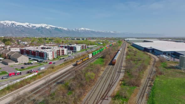 AERIAL - Train on railroad tracks with snow-capped mountains, Clearfield, Utah