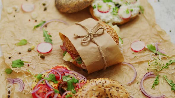 Bagels with Ham, Cream Cheese, Hummus, Radish Wrapped in Brown Baking Paper Ready for Take Away