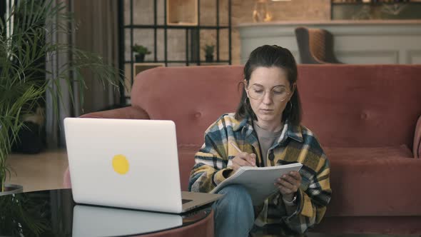 Serious Millennial Woman Taking Notes In Notebook While Using Laptop