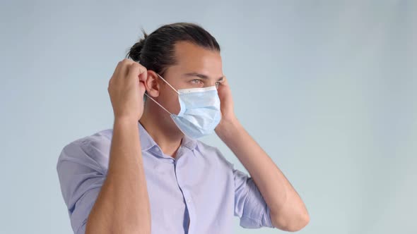 Man Puts on Face Mask Facing Right, Closeup with Grey Background and Copy Space