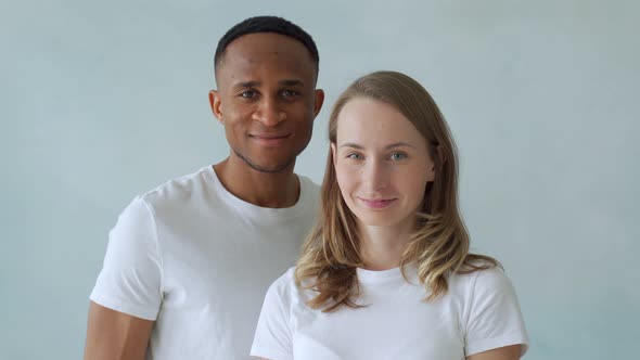 Young Interracial Couple Stand in White T-shirts and Smile at the Camera