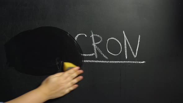 A woman's hand wipes off the word Deltacron written in chalk on the blackboard
