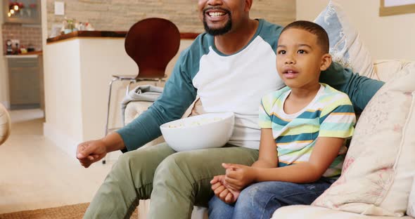 Father and son cheering up while watching television in living room 