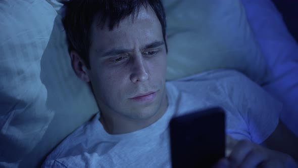 Man with Smarthone in a Bed at Night