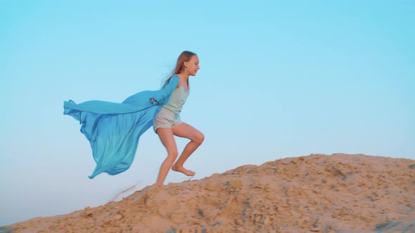 Playful Girl Teenager in Blue Pareo Walking on Sandy Hill in Summer Desert. Cheerful Girl in Blue