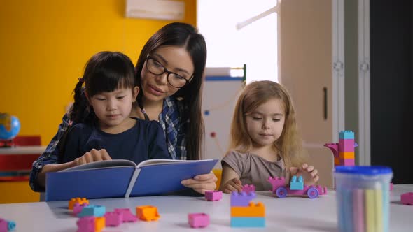 Preschool Asian Girl Reading Book with Teacher