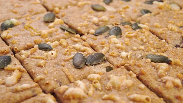 Crispy square grain rye crackers with pumpkin seeds and emmental cheese are stacked in rows. Macro