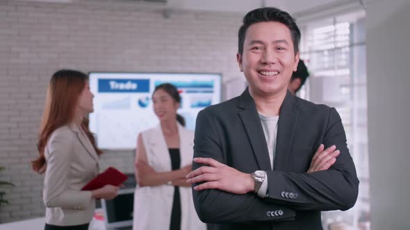 businessman standing with folded arms smiling at the camera in a boardroom with colleagues