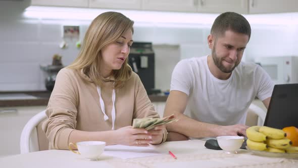 Caucasian Woman Counting Money Talking with Blurred Man Surfing Internet on Laptop at Background