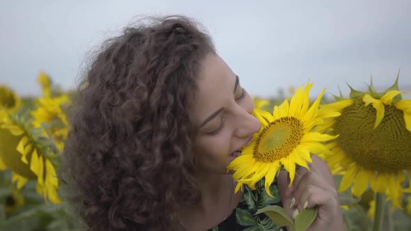 Portrait of Beautiful Curly Girl Jokingly Biting Big Sunflower in the Sunflower Field