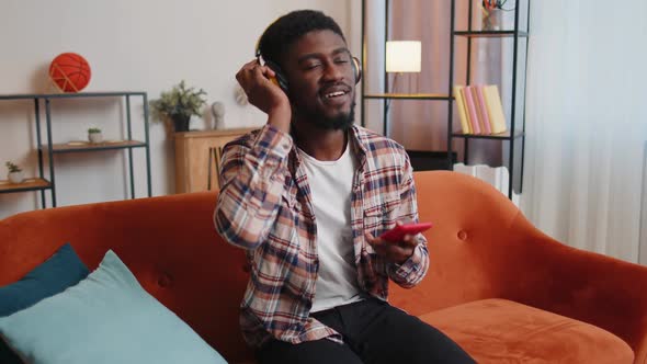 African American Young Man in Headphones Listening Music Dancing Singing in Living Room at Home