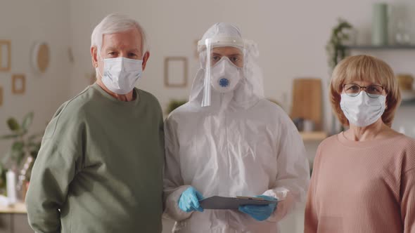 Portrait of Elderly Couple and Doctor in Protective Uniform at Home