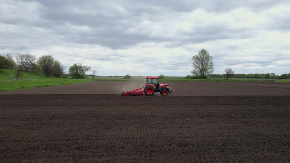 Aerial Shot of Tractor Plowing a Small Field with Blowing Dust in the Countryside of a Small Town