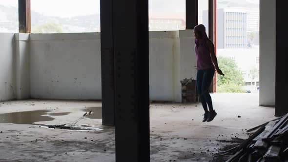 African american woman wearing hoodie skipping with rope in an empty urban building