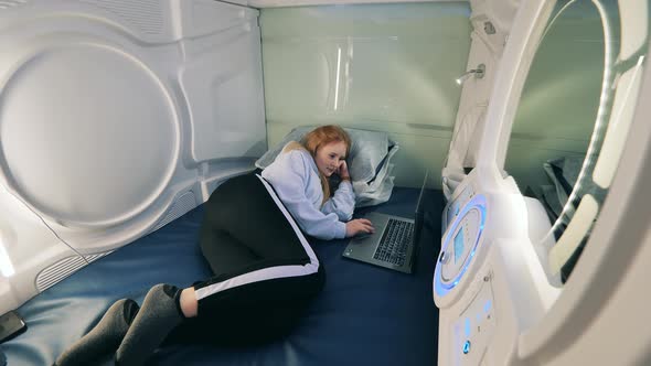Young Woman is Lying with a Laptop in the Capsule Hotel Room