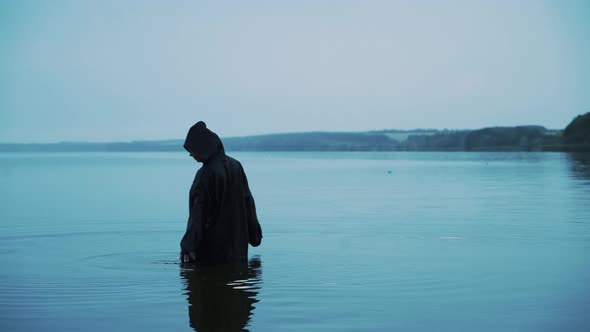 Evil witch in black cloak with hood in the river