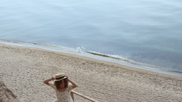 Joyful Woman Spinning Holding Straw Hat on Wooden Ladder Seashore Sunny Day