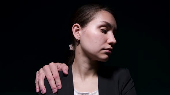 The hand of an unknown man lies on the shoulder of a young woman in a jacket