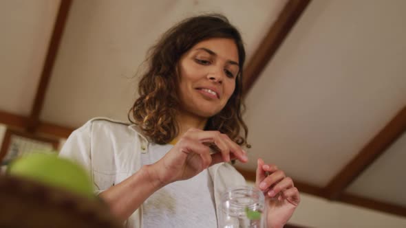 Happy mixed race woman preparing health drink standing in cottage kitchen smiling