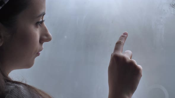 Young Woman Drawing a Heart on a Window