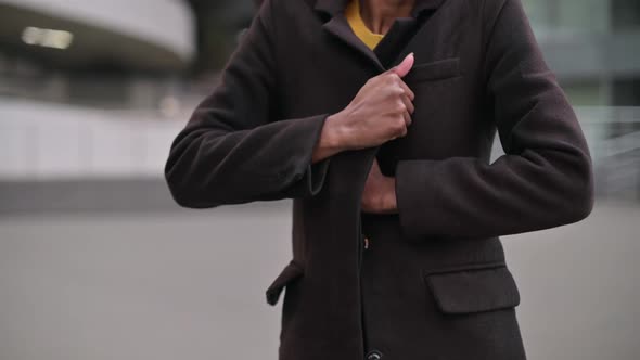 A black woman wraps her coat in windy, cool weather. Close-up