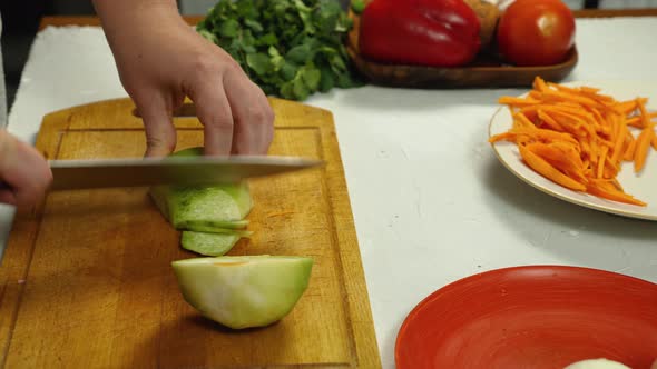 Close-up of a woman's hands taking a green radish off a plate and placing it on a kitchen board