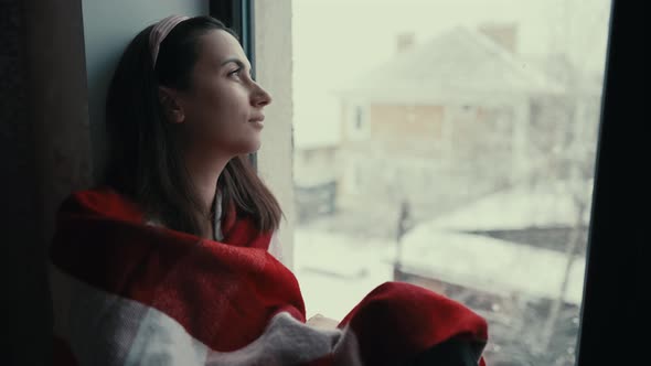 Sad Woman Looks Outside the Window Sitting on Windowsill