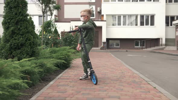 A boy stands in a mask near the house with a scooter and is sad.