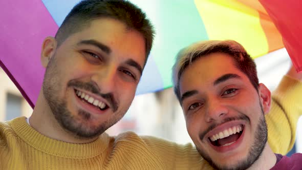 Young Gay Male Couple Under LGBT Rainbow Flag at Pride Parade Event