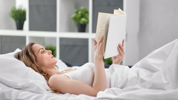 Relaxed Young Female Lying on Comfortable Bed Reading Book