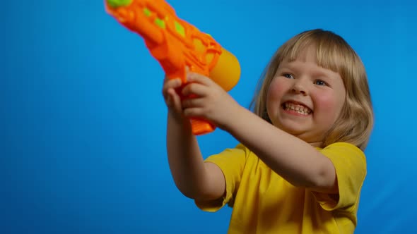 Little Blond Girl in Yellow Tshirt with Orange Water Gun is Laughing in Studio