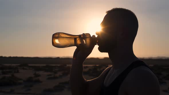 Young Sporty Man Drinking Water After Workout in Desert