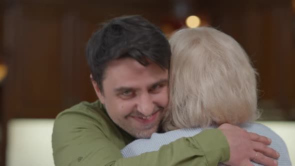 Closeup Portrait of Happy Adult Son Looking at Camera Smiling Hugging Greyhaired Senior Mother