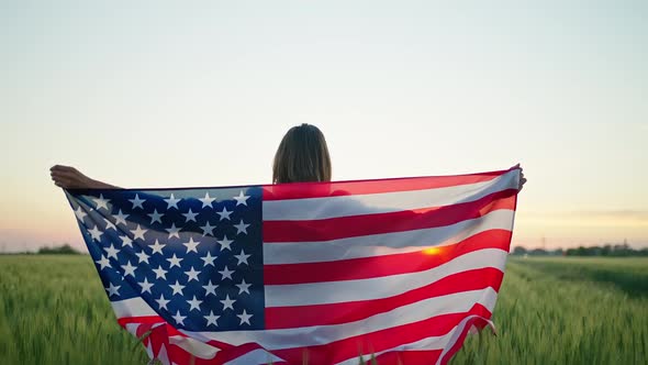 Rear View Slow Motion Footage of Woman in Field Puts Her Hands Up with the Flag of America