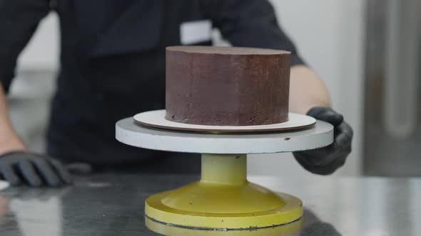 Blurred Caucasian Man in Coronavirus Face Mask Examining Round Chocolate Cake on Rotating Table