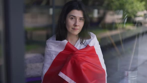 Happy Woman Wrapping in Canadian Flag Looking at Camera Smiling Standing Indoors