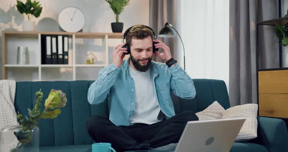 Man Sitting on Comfortable Sofa at Home and Enjoying Music from Phone Playlist Using Headphones