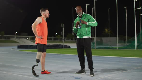 Diverse male coach and disabled male athlete with running blade standing and talking