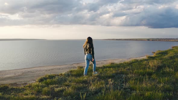 Tracking Aerial Shot of Young Woman Enjoying Sunset in Field Near the Cliff During Beatiful Sunset