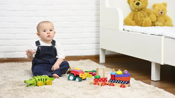 Baby Boy in Denim Overalls Plays with Toys