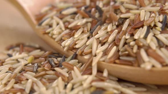 Mixed basmati integral rice falls into a heap in a wooden spoon on a board in slow motion