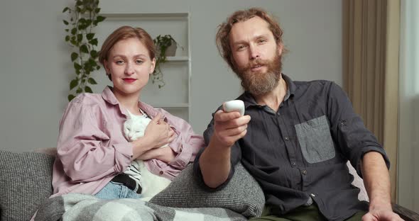 Young Caucasian Couple Watching TV Movie Program with Cat Pet Kitten Animal Relax Enjoying Rest at