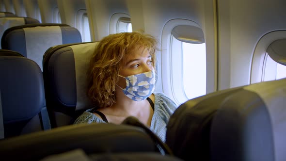 a Girl in a Fashionable Cheerful Trendy Mask is Sitting in an Airplane at the Window