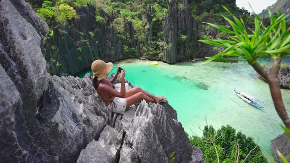 Woman Sitting On Limestone Rocks Taking Photo With Smartphone