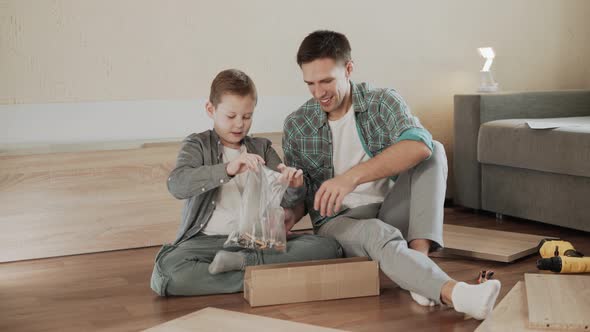 Dad and Son Sit on Floor and Take Out Fittings to Assemble Cabinet From Box