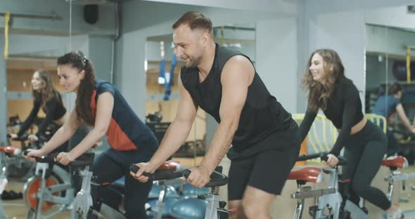 Happy Athletic Men and Women Cycling Exercise Bikes in Gym. Side View Portrait of Cheerful Young alt
